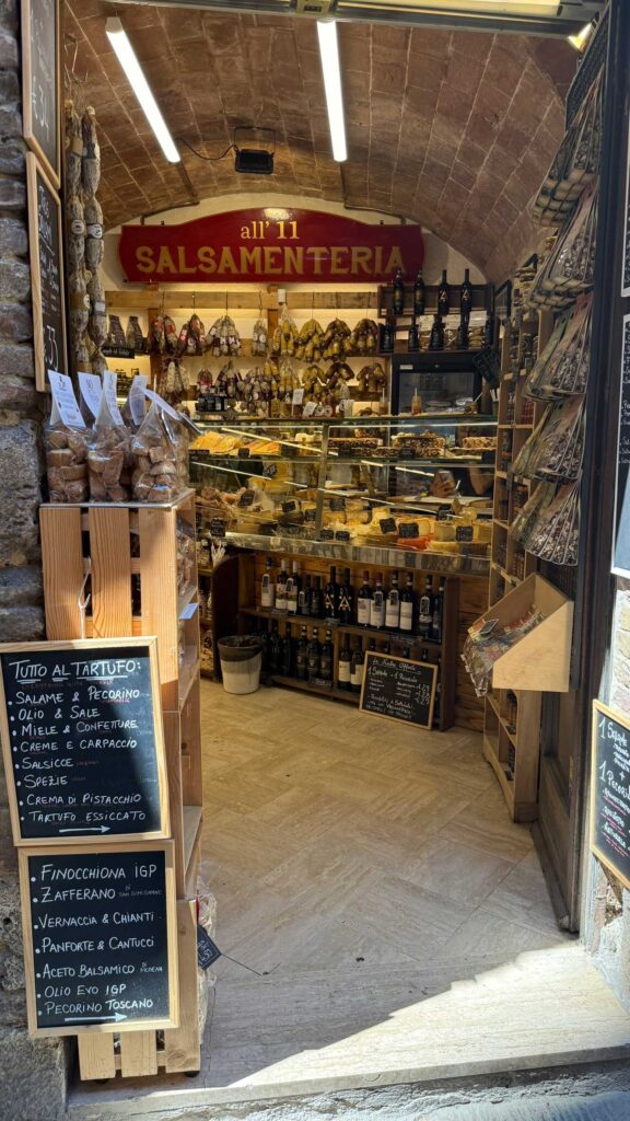 Helyi delikáteszüzlet San Gimignanóban pecorino sajtokkal, toszkán szalámikkal és Vernaccia borokkal